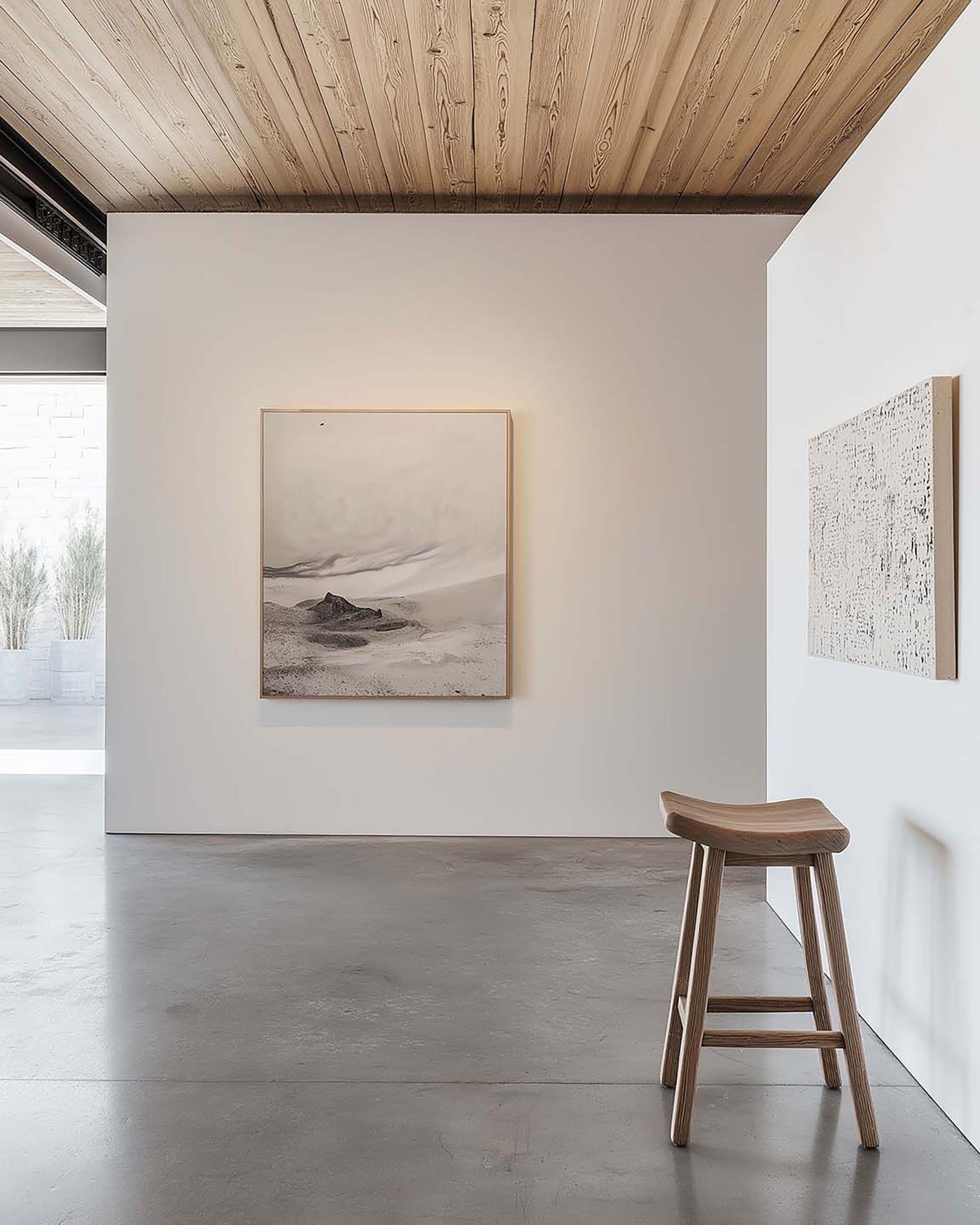 Minimal hallway gallery wall with a square frame on a white wall, warm wood ceiling above and a wooden stool nearby.