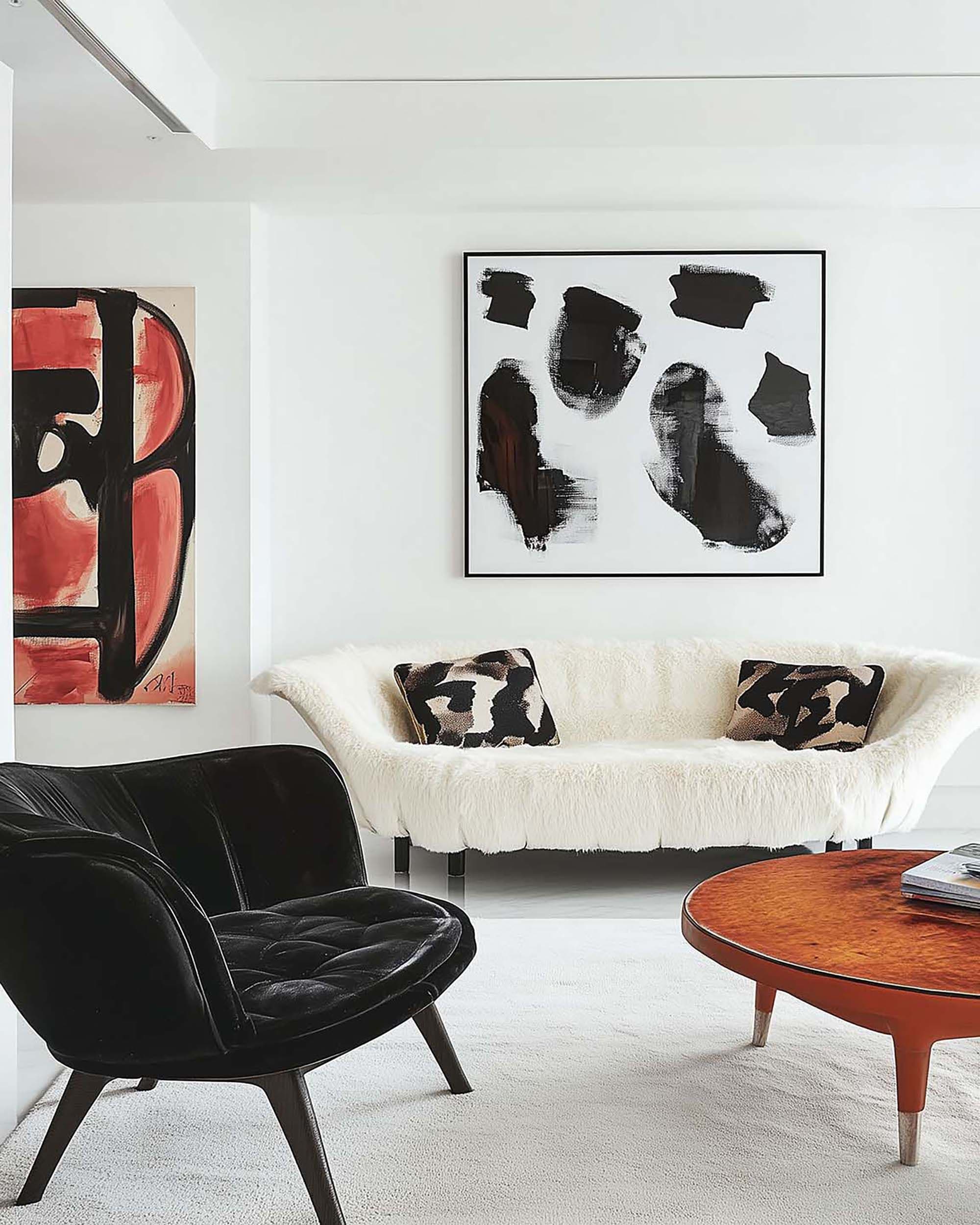 Bright modern living room with a black-framed wall art piece centered above a white sofa and a round wood coffee table.