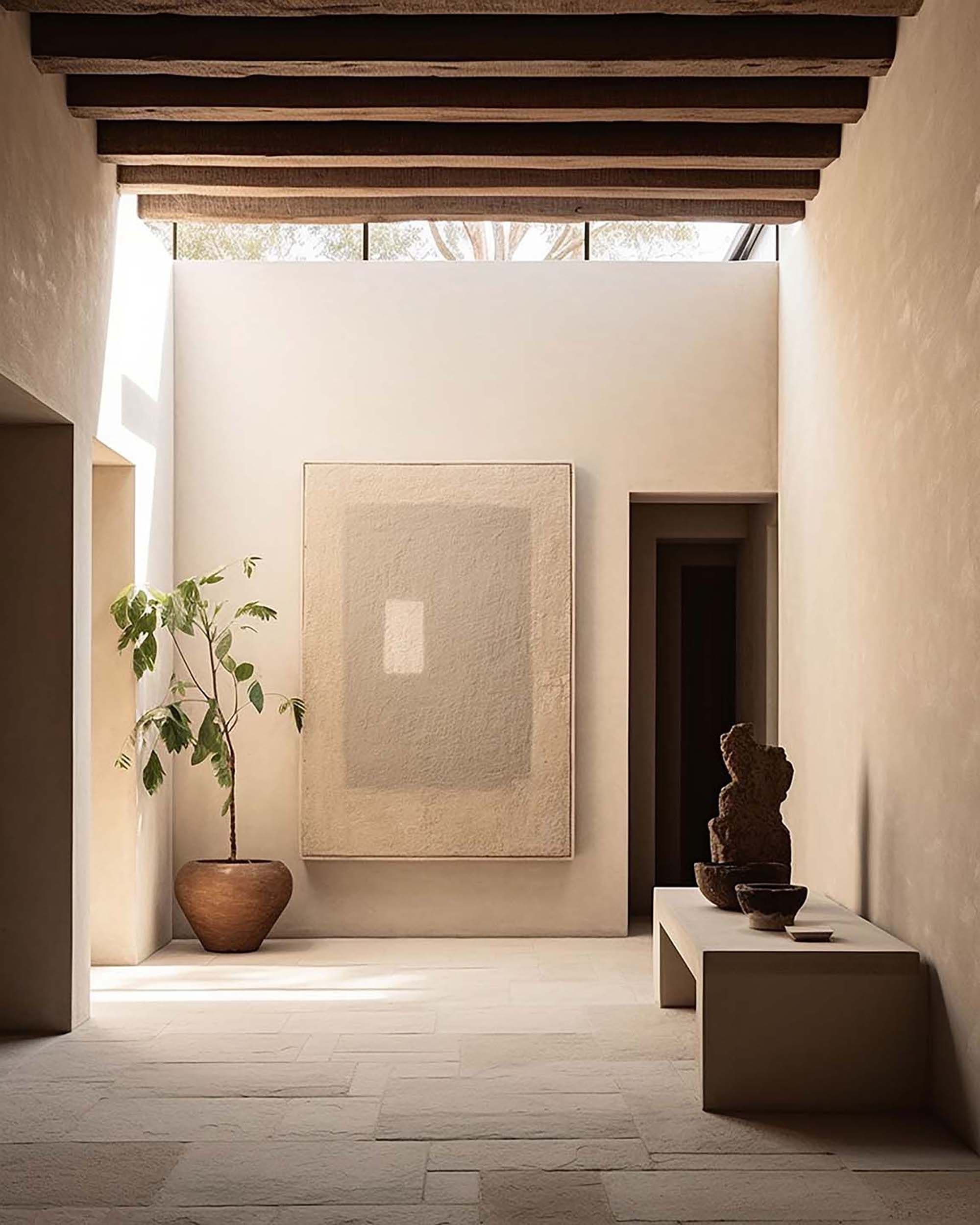 Minimalist hallway with a large wall-hung frame on a plaster wall, plus a potted tree and a low bench.