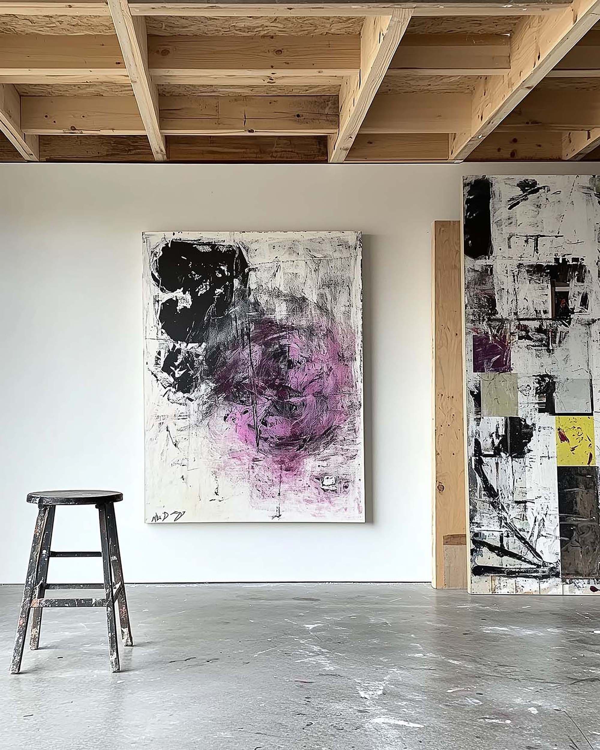 Industrial artist studio wall with a large customizable frame centered on a white wall beside a worn black stool.