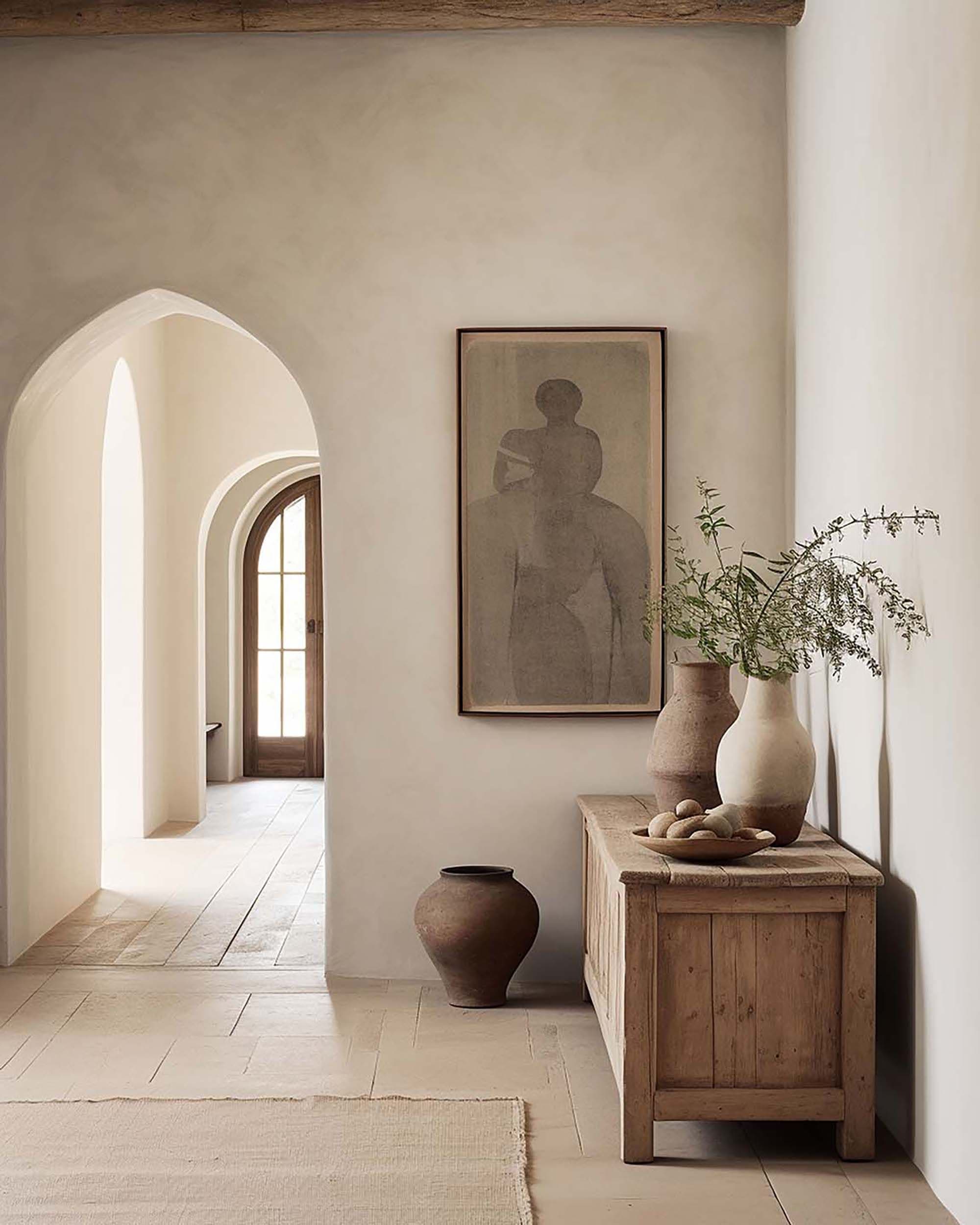 Arched hallway with a wall-mounted frame above a rustic wood console table with ceramic vases and greenery.