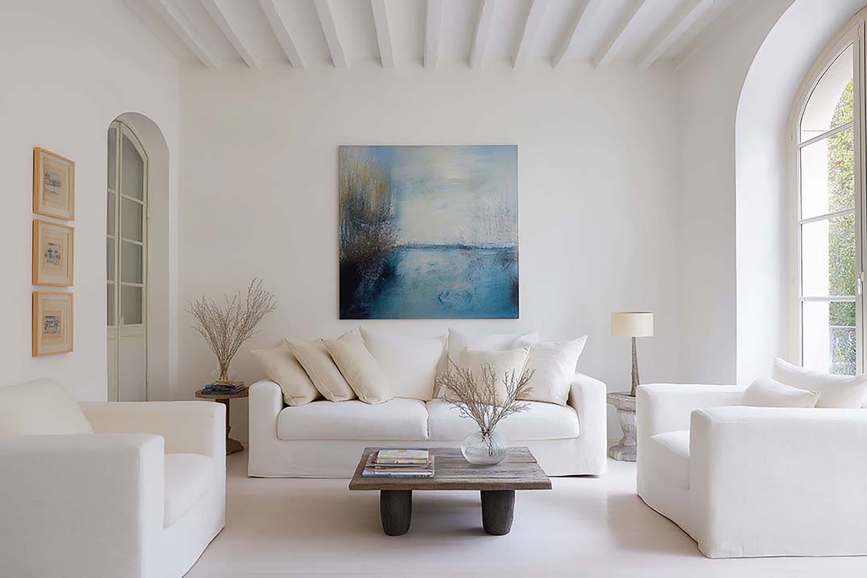 Bright minimalist living room with a large wall art spot above a white sofa, plus a low wood coffee table.