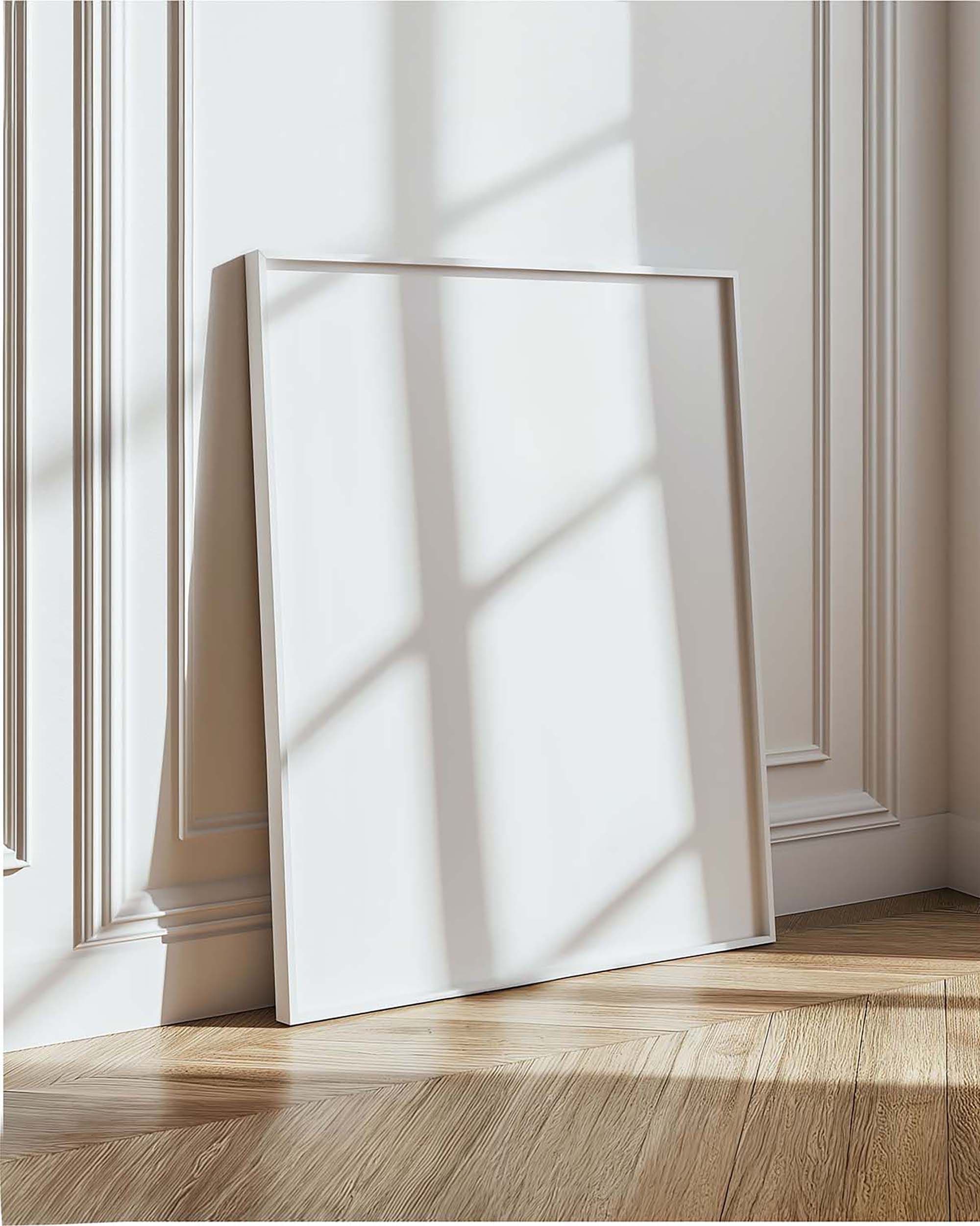Leaning white frame on a paneled wall in a bright living room corner with warm wood floors and window shadows.