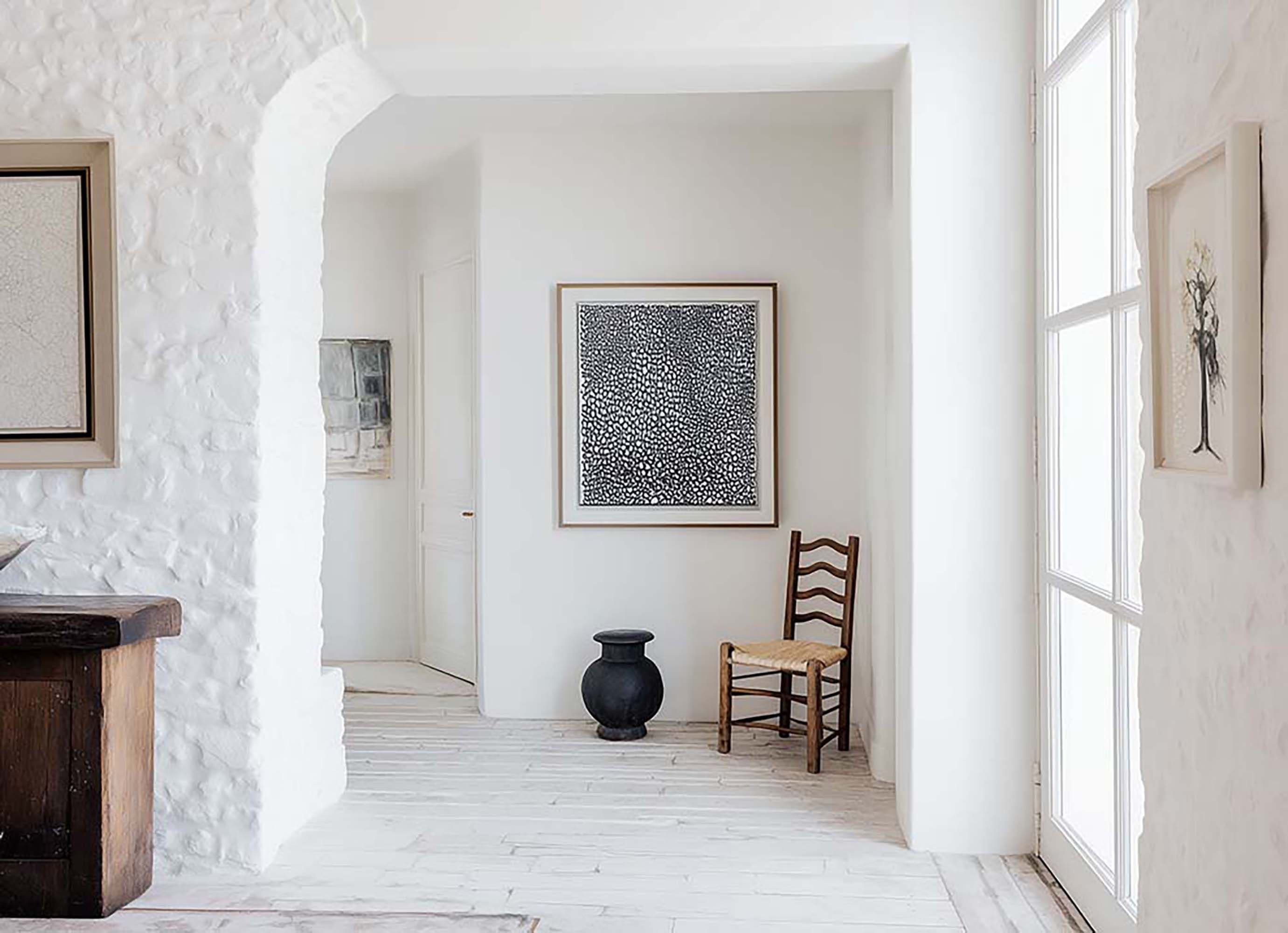 Bright hallway with a framed artwork centered on a white wall, next to a wooden chair and a small black vase.