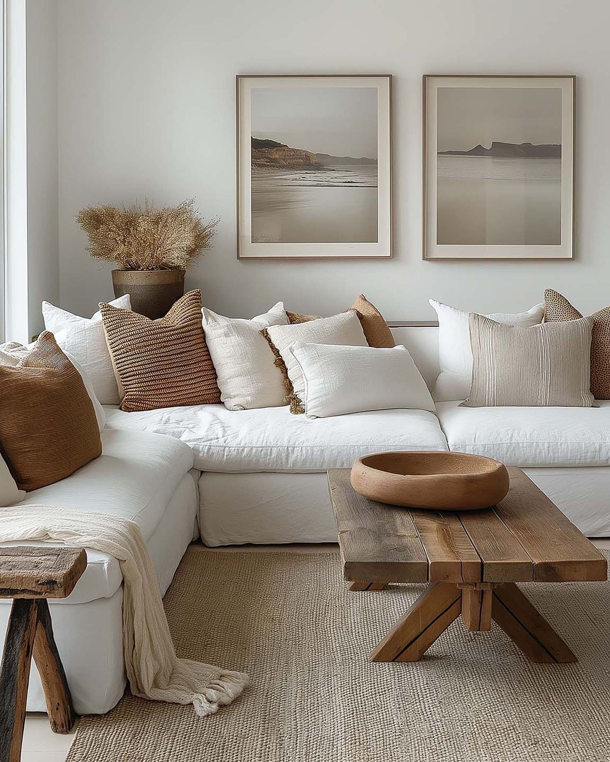 Neutral living room with two framed artworks above a white sectional sofa, a rustic wood coffee table, and a woven rug.