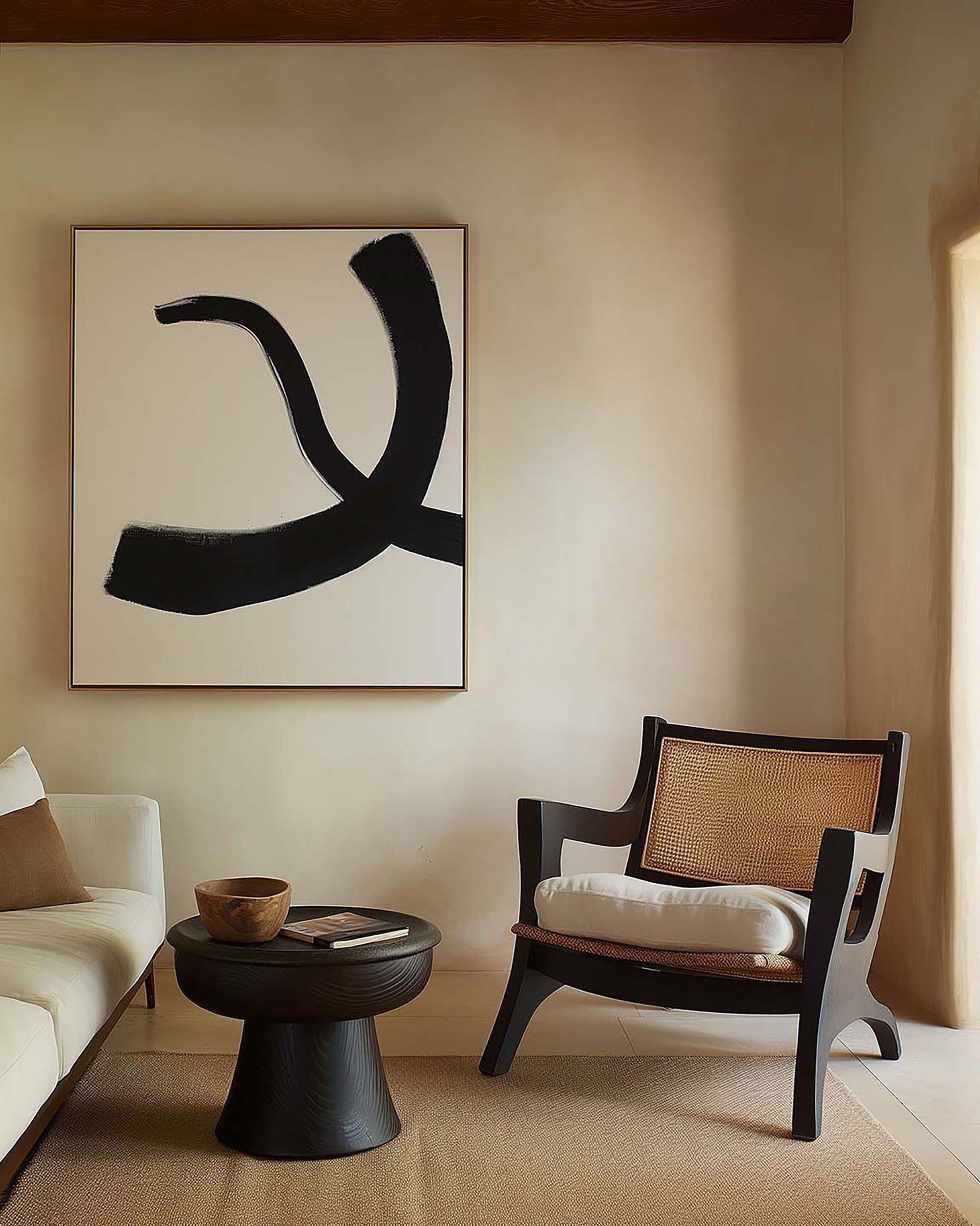Minimalist living room with a large wall-hung frame above a black round side table, next to a cane-back chair.