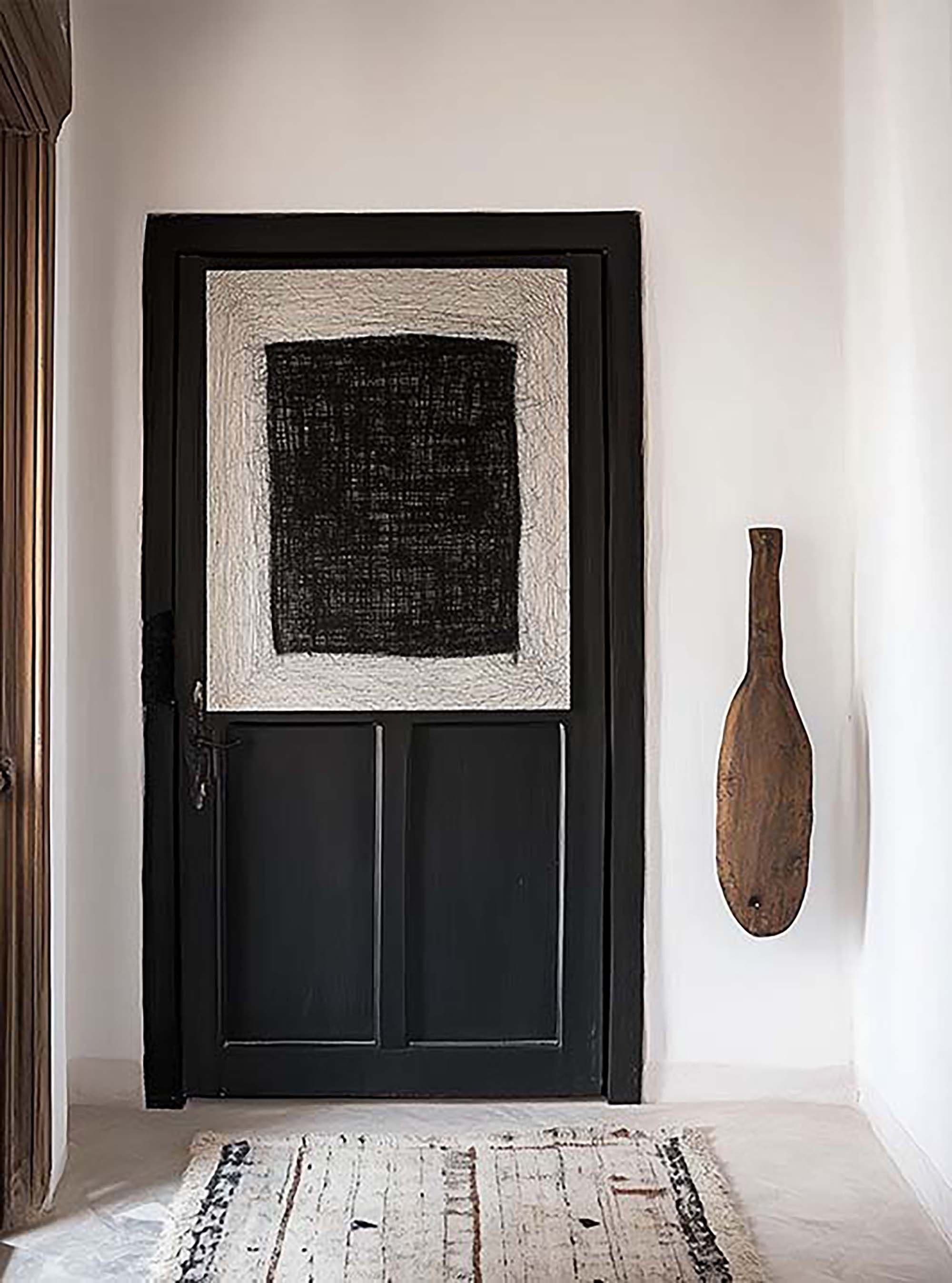 Minimal entryway with a large black frame leaning against a black paneled door, next to a wall-mounted wooden paddle.