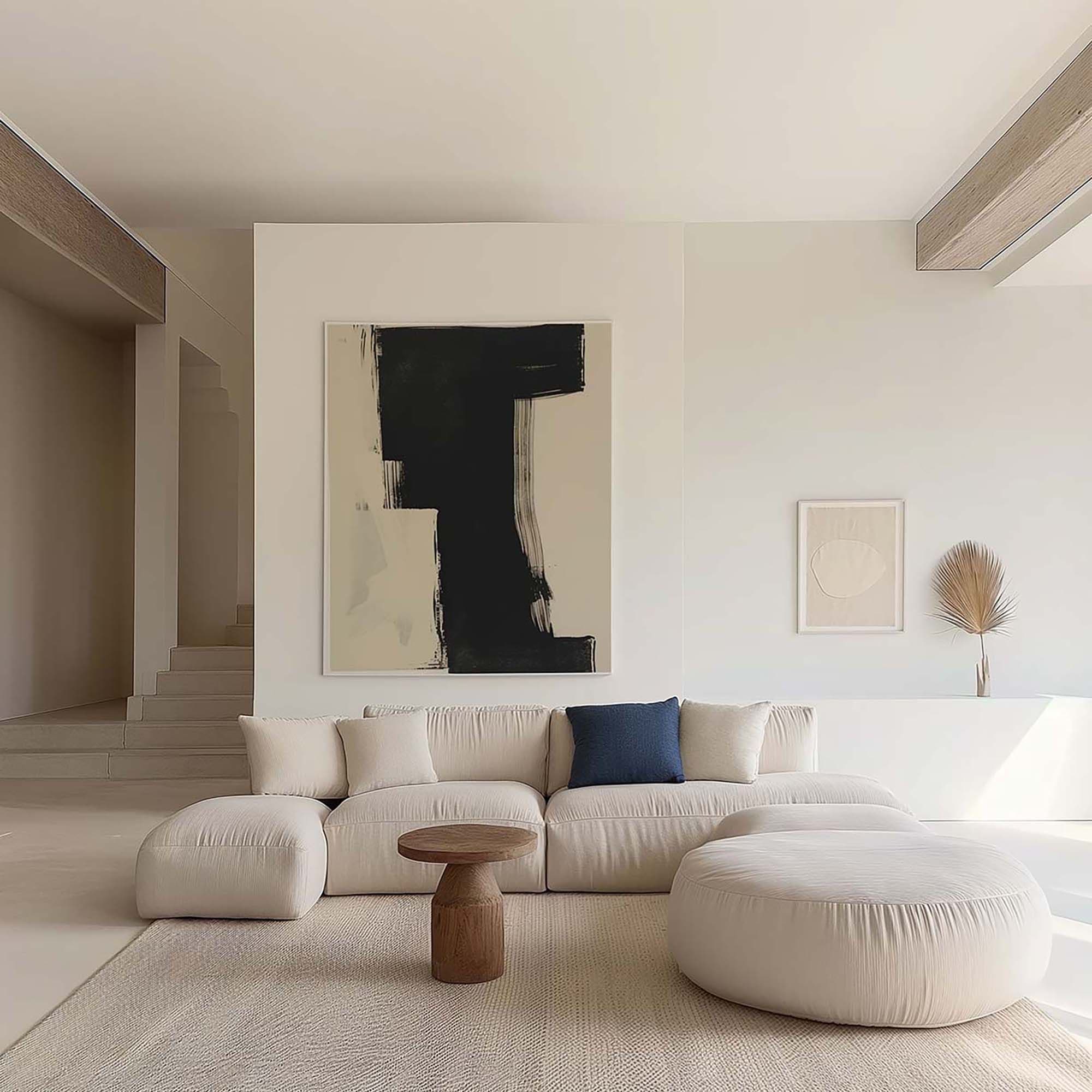 Minimal living room with a large framed artwork centered above a low cream sectional sofa and a small round wood coffee table.