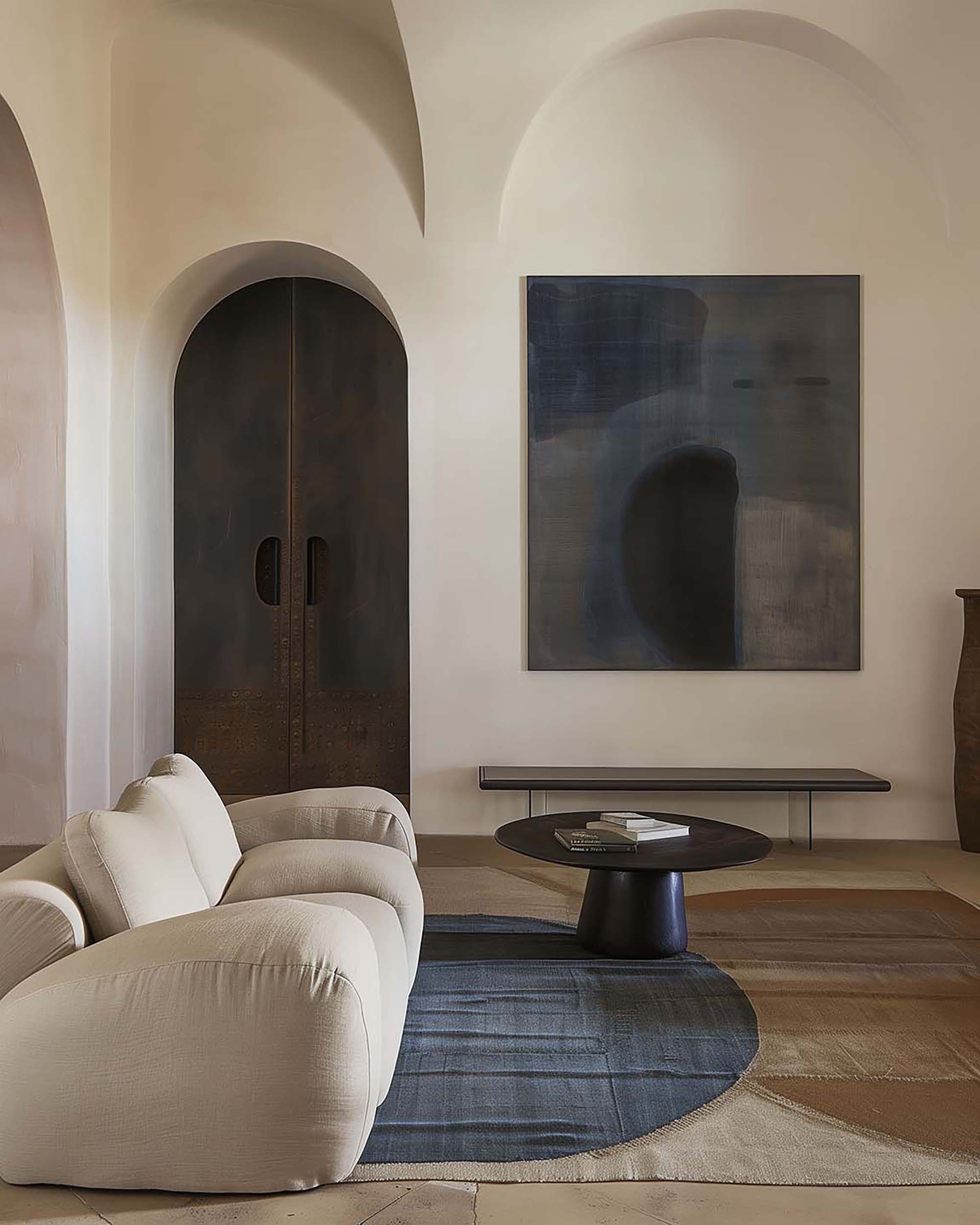 Neutral living room with a large wall frame above a low bench, beside an arched dark wood door and a cream sofa.