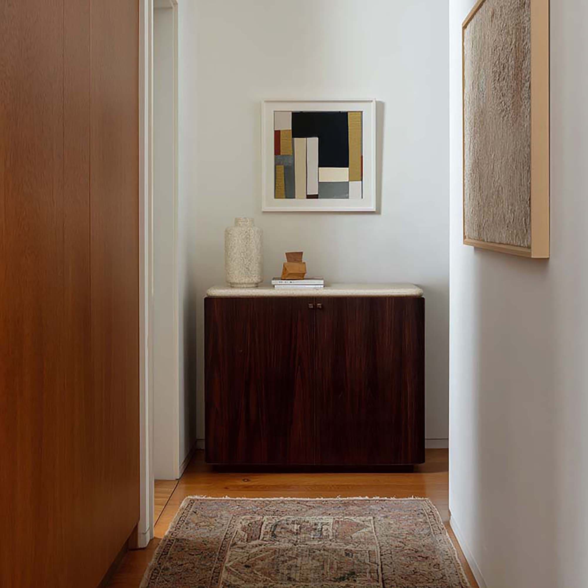 Hallway wall with a framed print above a dark wood sideboard, with a small rug on the wood floor.