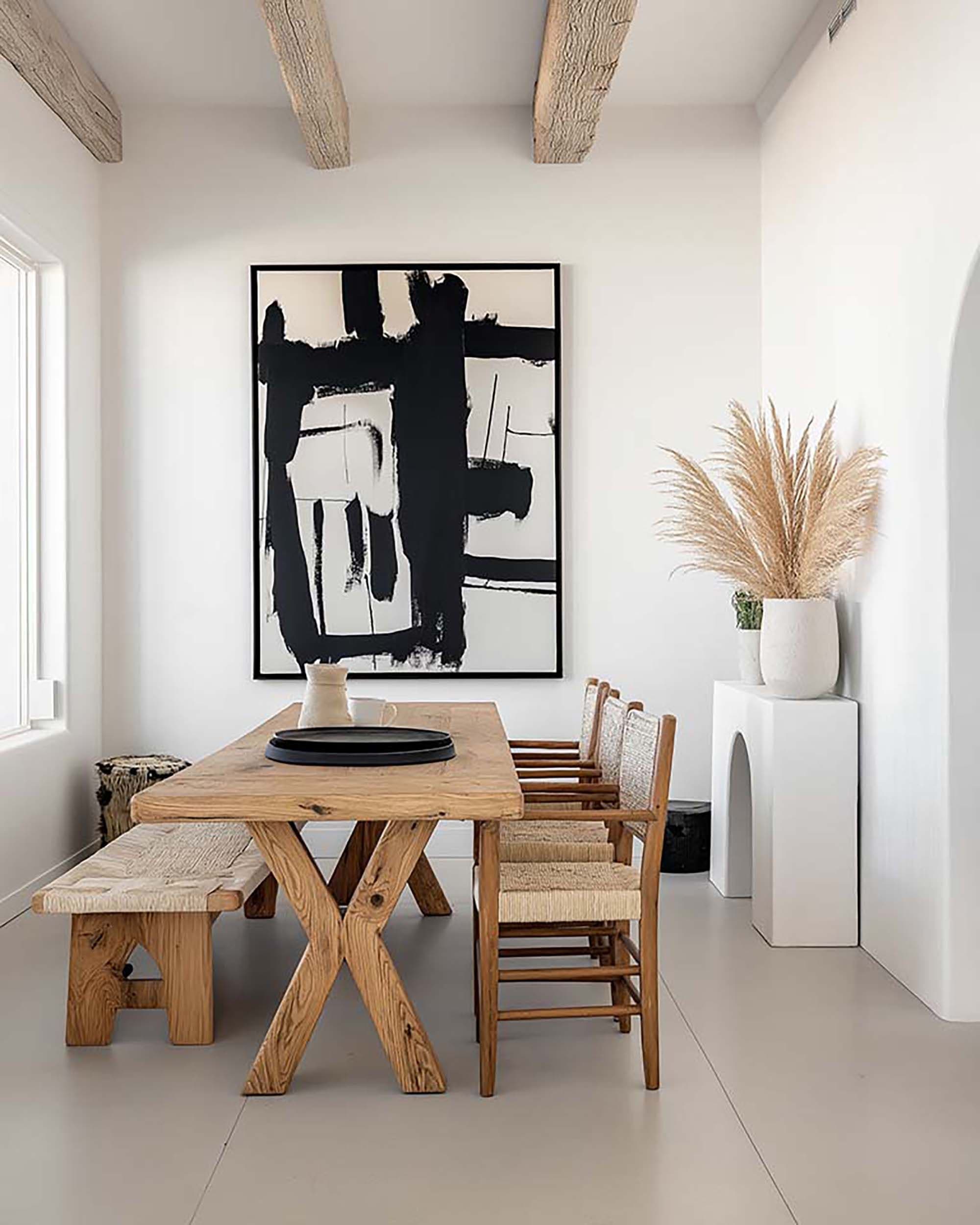 Minimal dining room with a large black-framed wall art above a wood table, with exposed ceiling beams overhead.