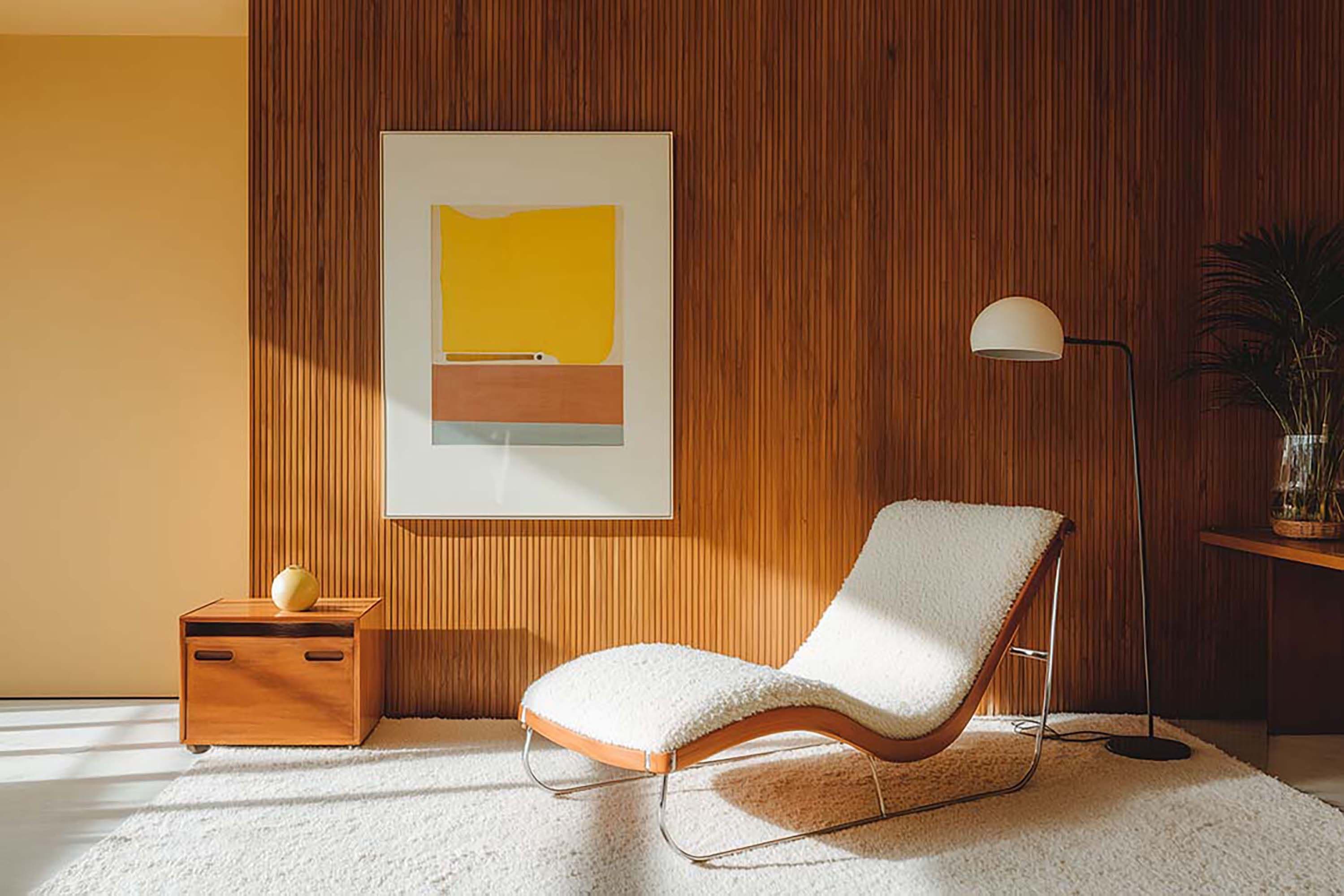 Living room with a framed wall print on a vertical slat wood accent wall above a low wood cabinet and a lounge chair.
