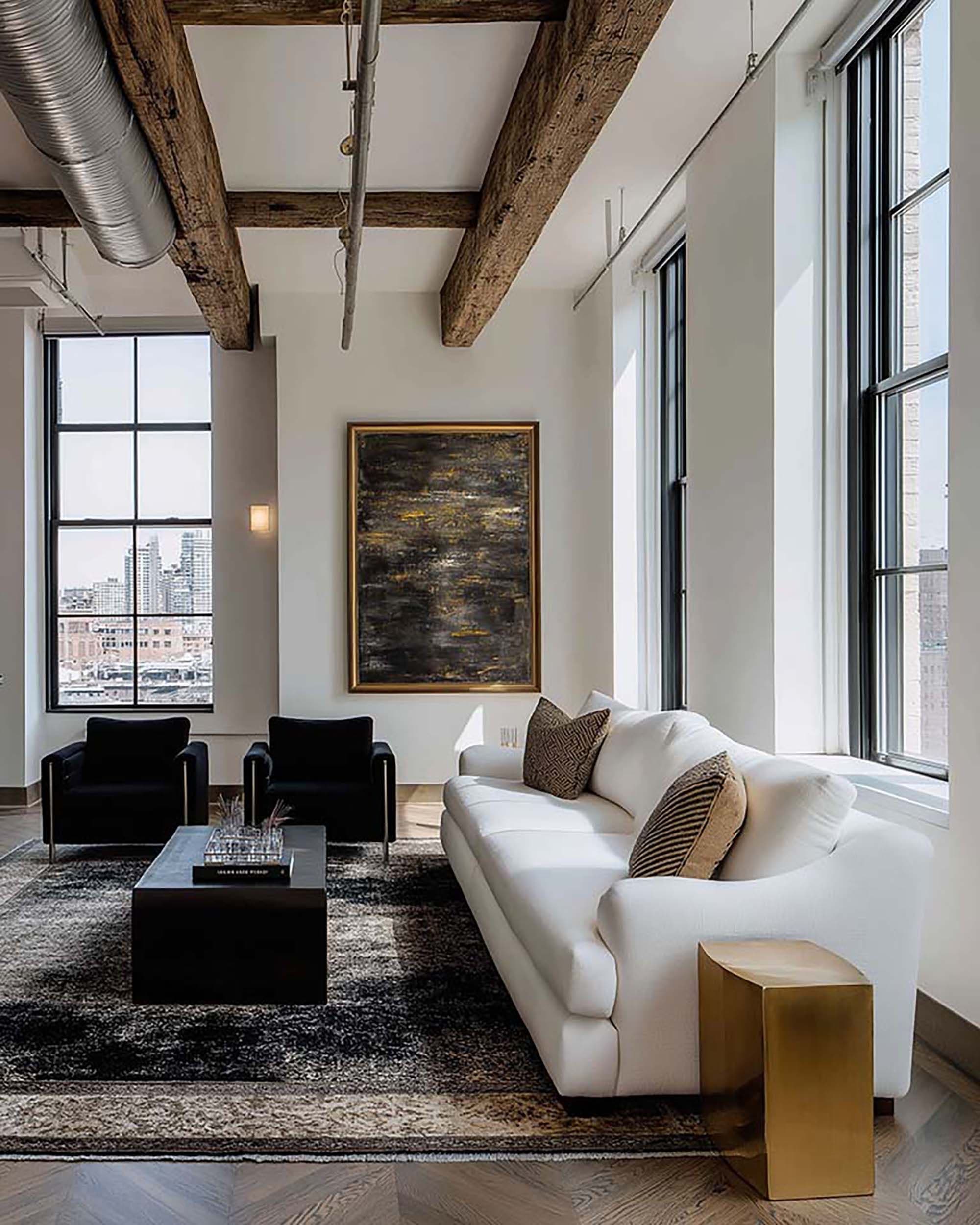 Industrial loft living room with a large framed wall piece above two armchairs, beside a white sofa and coffee table.
